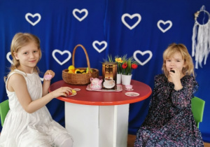 Dwie dziewczynki siedzą przy stoliku i piją herbatkę.
